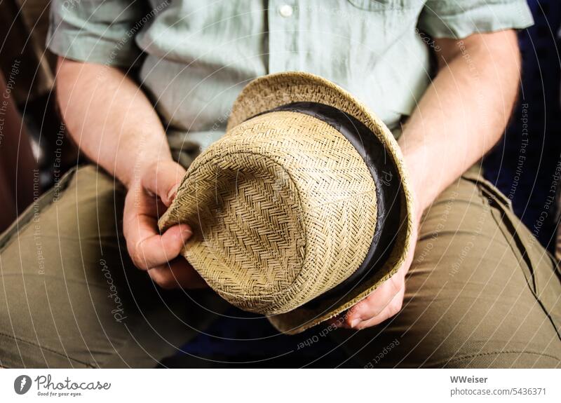 Ein sommerlich gekleideter Mann hält seinen hellen Strohhut in den Händen Hut Sommerhut sitzen Herr Saison Kopfbedeckung Sonne Hitze heiß Licht Schutz schützen