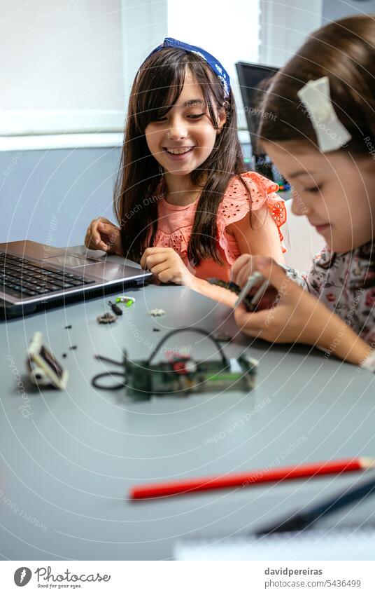 Glückliche Studentin lächelt, während sie einem Klassenkameraden beim Zusammenbau von Maschinenteilen zusieht Frau Schüler Lächeln Blick Kinder versammeln