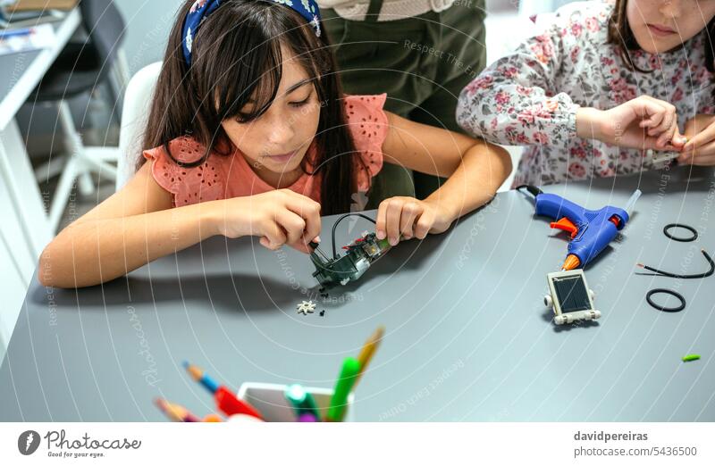Studentin schraubt elektrischen Schaltkreis neben ihrem Lehrer und einem Schulkind im Robotikunterricht Schüler Kinder Frau Verschraubung schrauben elektronisch