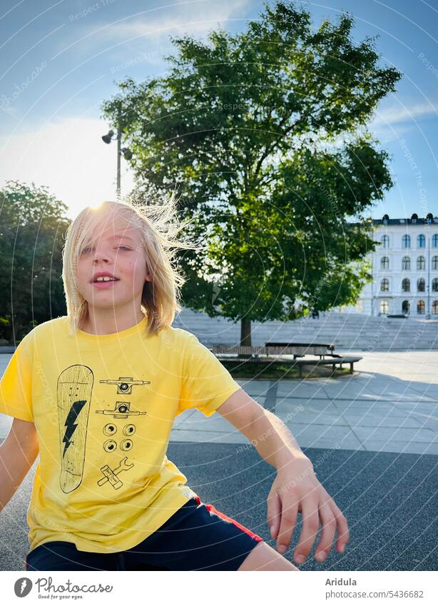 Junge im Wind in der Stadt Kind Haare Bewegung gelb Baum Platz Mensch Jugendliche Porträt Haare & Frisuren öffentlicher Raum Asphalt Gegenlicht Sommer Gesicht