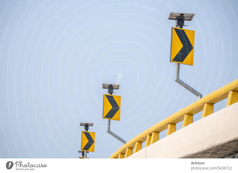 Gelbe Verkehrsschilder weisen den Autofahrern den Weg über kurvenreiche Straßen. Symbole sorgen für Sicherheit, während sie unter dem wachsamen blauen Himmel über die Straßen fahren. Pfeilzeichen auf einem Autobahnschild vor blauem Himmel.