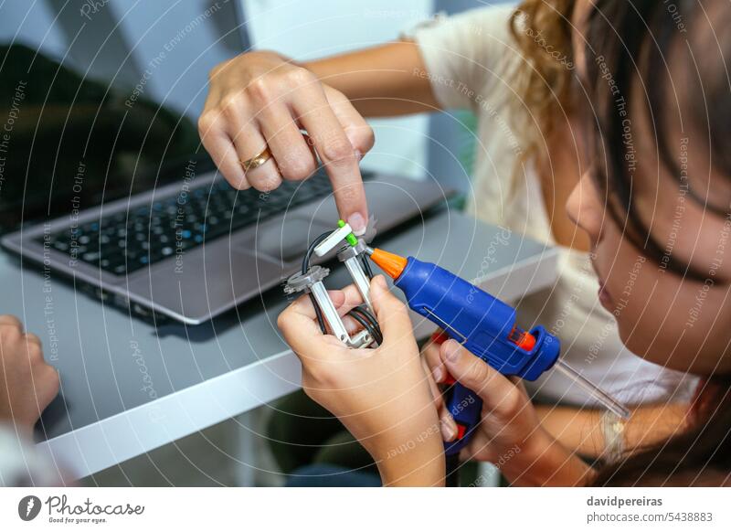 Lehrer hilft einem Schüler bei der Verwendung einer Heißklebepistole für Maschinenteile im Robotikunterricht unkenntlich Frau Hilfe unterstützen abstützen Kind