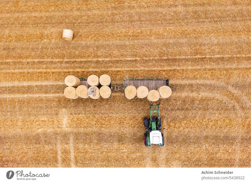 Luftaufnahme eines Traktors mit Mistgabel, der Heuballen auf einen Anhänger lädt Stoppelfeld Ernte Forke laden trocknen Herbst Feld Strohballen Muster