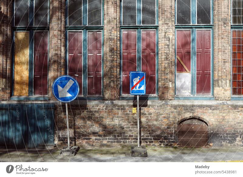 Blaue Verkehrszeichen im Sonnenschein vor einer alten Fassade aus Backstein mit alten Fenstern in den Gassen der Altstadt von Brügge in Westflandern in Belgien