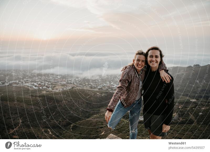 Südafrika, Kapstadt, Kloof Nek, Porträt von zwei glücklichen Frauen, die sich bei Sonnenuntergang umarmen Umarmung Umarmungen Arm umlegen weiblich Freundin