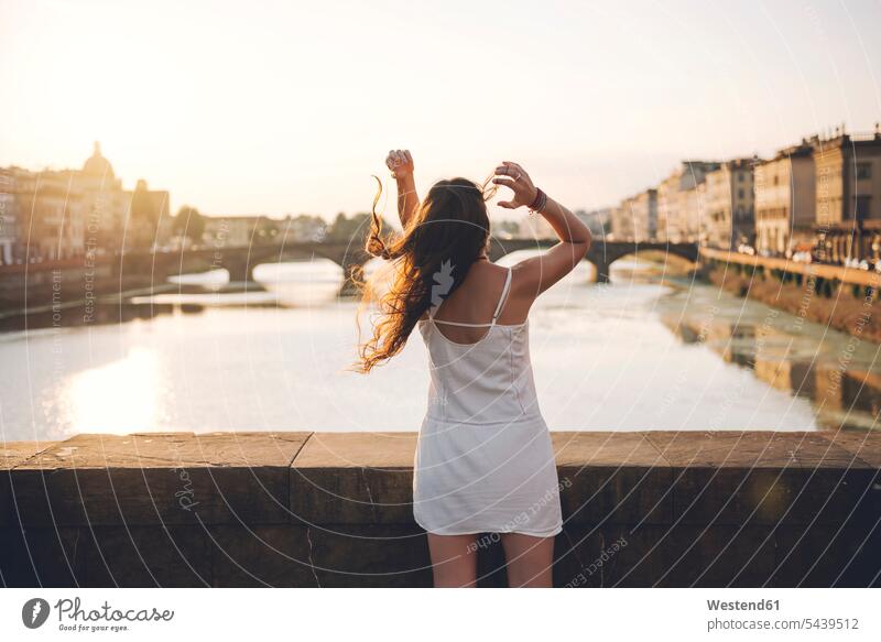 Italien, Florenz, Rückenansicht einer Frau in weißem Sommerkleid, die bei Sonnenuntergang auf einer Brücke steht Gegenlicht Gegenlichtaufnahmen glücklich Glück