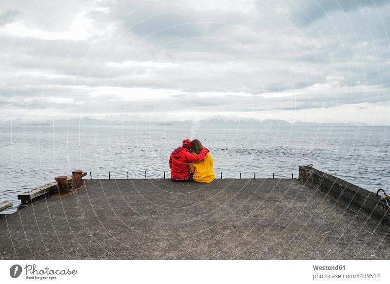Island, nördlich von Island, Rückenansicht eines Paares, das auf dem Steg sitzt und auf die Aussicht schaut ansehen Ausblick Ansicht Überblick Pärchen