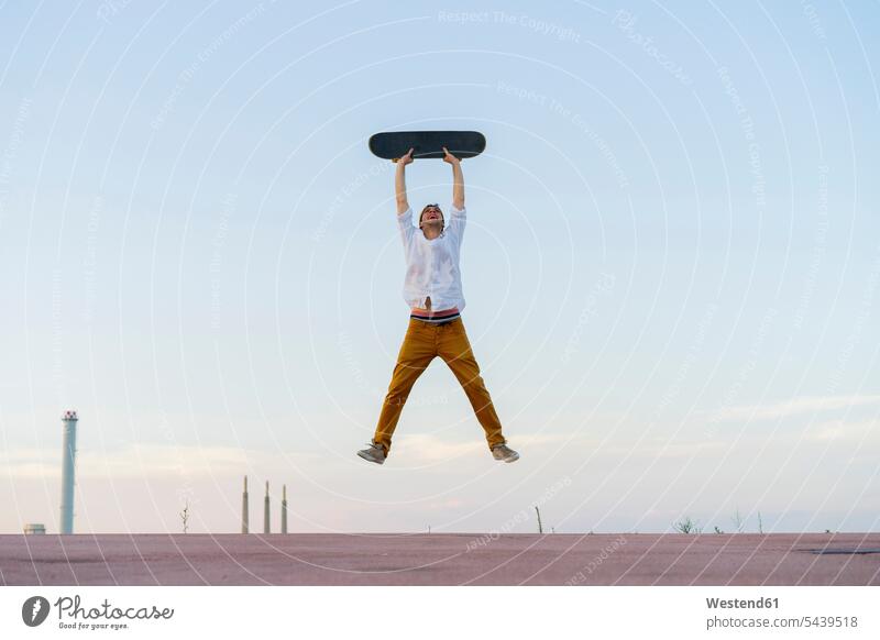 Junger Mann springt in die Luft und hält ein Skateboard springen hüpfen Rollbretter Skateboards halten Männer männlich Sprung Spruenge Sprünge Erwachsener