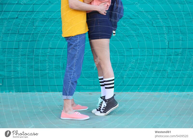 Junges Paar küsst sich vor einer blauen Ziegelmauer, Teilansicht Pärchen Paare Partnerschaft Mensch Menschen Leute People Personen küssen Küsse Kuss Bein Beine