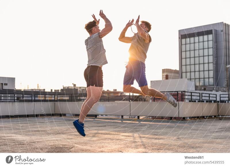 Freunde spielen bei Sonnenuntergang auf einem Dach Basketball Basketbaelle Basketbälle springen hüpfen jung Luftsprung Luftsprünge einen Luftsprung machen