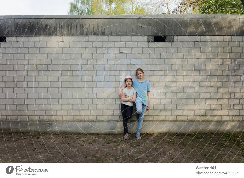 Porträt von zwei Mädchen, die an einer Ziegelmauer stehen Freunde Kameradschaft Freundin T-Shirts Arm umlegen Umarmung Umarmungen stehend steht Muße Miteinander