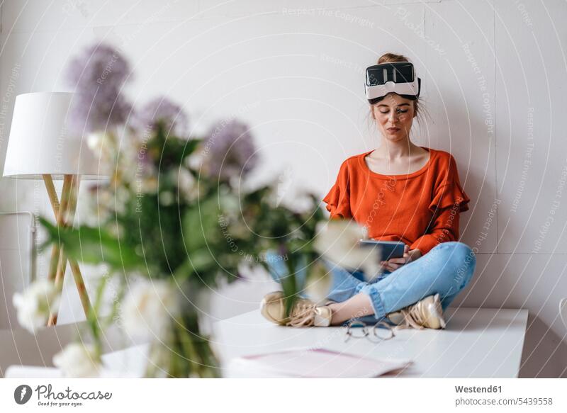 Junge Frau, die mit einem Tablett auf einem Tisch sitzt und eine VR-Brille trägt Blume Blumen Blüte Vase Vasen Tablet Computer Tablet-PC Tablet PC iPad