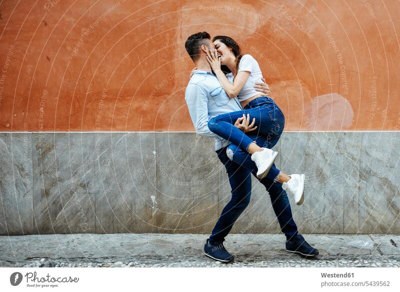 Sorgenfreies verliebtes Paar vor einer Mauer im Freien Liebe lieben Unbeschwert Sorglos Pärchen Paare Partnerschaft Wand Wände Waende positiv Emotion Gefühl