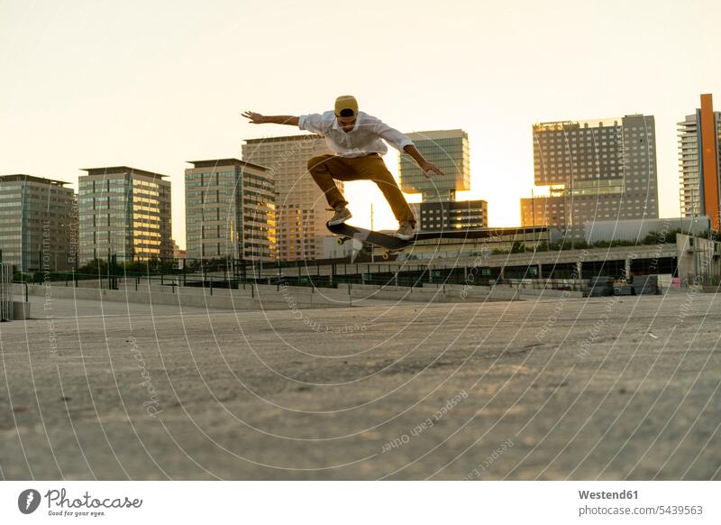 Junger Mann macht einen Skateboard-Trick in der Stadt bei Sonnenuntergang Skateboarder Skateboardfahrer Skateboarders Skater staedtisch städtisch Rollbretter