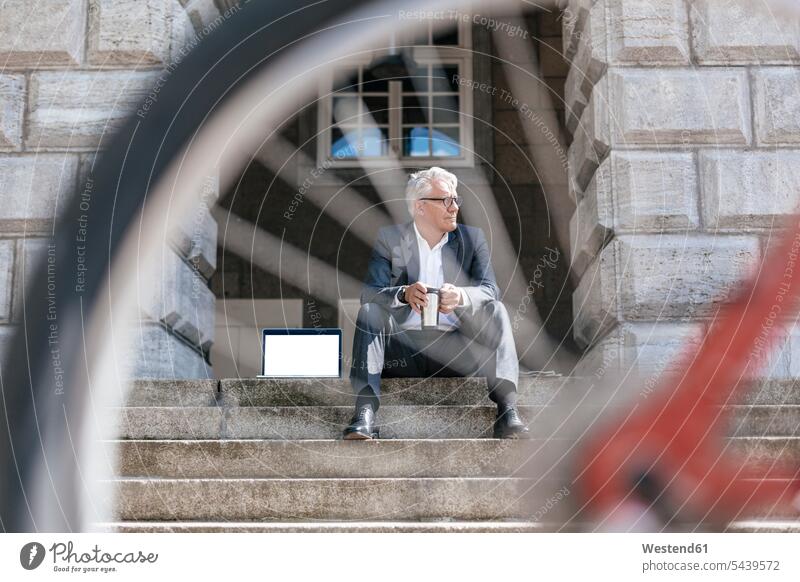 Älterer Geschäftsmann mit Fahrrad, der mit Laptop und Reisetasse auf einer Treppe im Freien sitzt Notebook Laptops Notebooks Businessmann Businessmänner