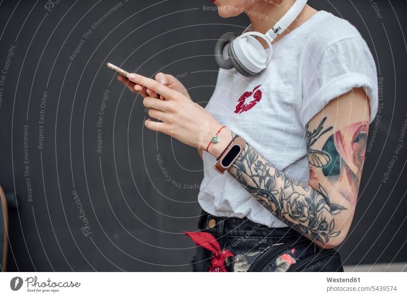 Nahaufnahme einer tätowierten jungen Frau mit Kopfhörern, die ein Mobiltelefon benutzt Kopfhoerer cool Coolness weiblich Frauen Handy Handies Handys
