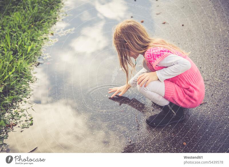 Kleines Mädchen spielt mit dem Wasser einer Pfütze Landshut Tag tagsueber Tageslichtaufnahme tagsüber am Tag Tageslichtaufnahmen Tagesaufnahmen Freizeitkleidung
