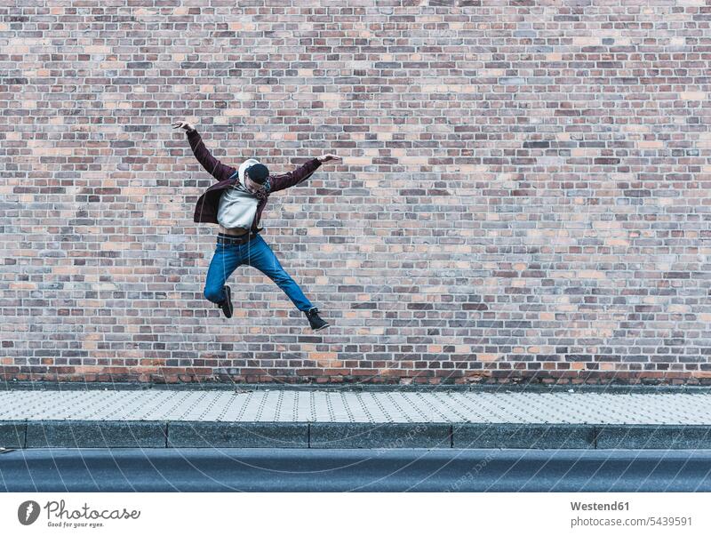 Junger Mann springt vor Ziegelmauer springen hüpfen Männer männlich Sprung Spruenge Sprünge Erwachsener erwachsen Mensch Menschen Leute People Personen Gehsteig