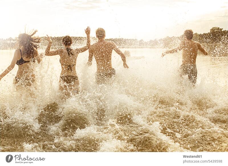 Vier Freunde laufen in einen Baggersee spritzen genießen geniessen Genuss Gemeinsam Zusammen Miteinander nebeneinander Seite an Seite Bewegung sich bewegen