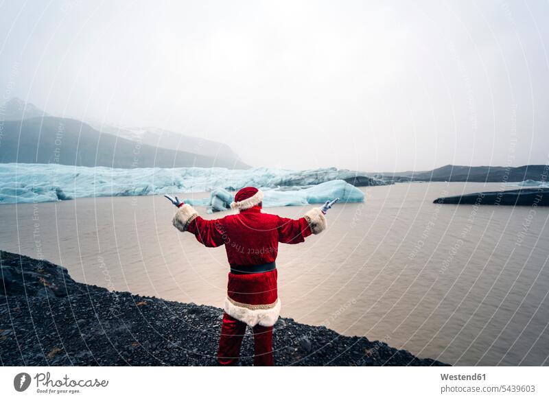 Island, Rückansicht des Weihnachtsmanns vor Gletscher stehend Weihnachtsmänner Weihnachtsmaenner Santa Claus Nikolaus Eis Ice Weihnachten Christmas X-Mas X mas