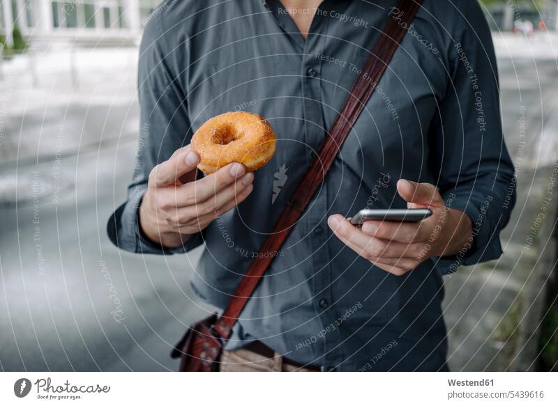 Hände eines Geschäftsmannes mit Doughnut und Smartphone, Teilansicht Donut Donuts Doughnuts halten iPhone Smartphones Hand Businessmann Businessmänner