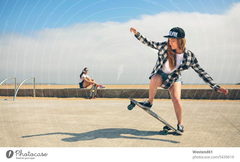 Junge Frau beim Longboarding, während ihre Freundin sie beobachtet Skateboarderin Skateboardfahrerin Skaterin Skateboarderinnen Skaterinnen
