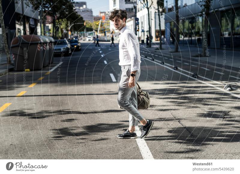 Junger Mann in der Stadt auf dem Sprung über die Straße staedtisch städtisch Strassen Straßen unterwegs auf Achse in Bewegung überqueren Männer männlich gehen
