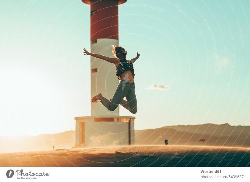 Junge Frau springt in Wüstenlandschaft am Leuchtturm Leuchttürme springen hüpfen weiblich Frauen Landschaft Landschaften Turm Türme Tuerme Bauwerk Gebäude