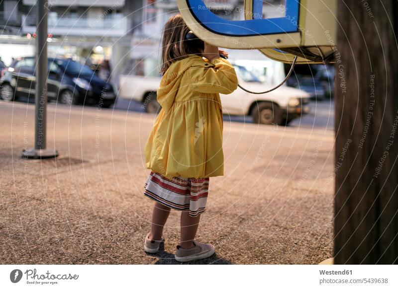 Rückansicht eines kleinen Mädchens bei der Benutzung einer Telefonzelle weiblich Telefonzellen Telefonhaeuschen Telefonhäuschen benutzen benützen Kind Kinder