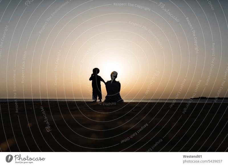 Spanien, Menorca, Silhouette von Mutter und Sohn beim Anblick des Sonnenuntergangs an der Strandpromenade Bodenhöhe Froschperspektive Bodenhoehe Natur Reiseziel