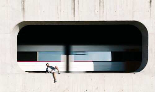Spanien, Tarragona, entspannter junger Mann in der Nische einer Betonmauer mit einem fahrenden Zug im Hintergrund Europäer Kaukasier kaukasisch Europäisch