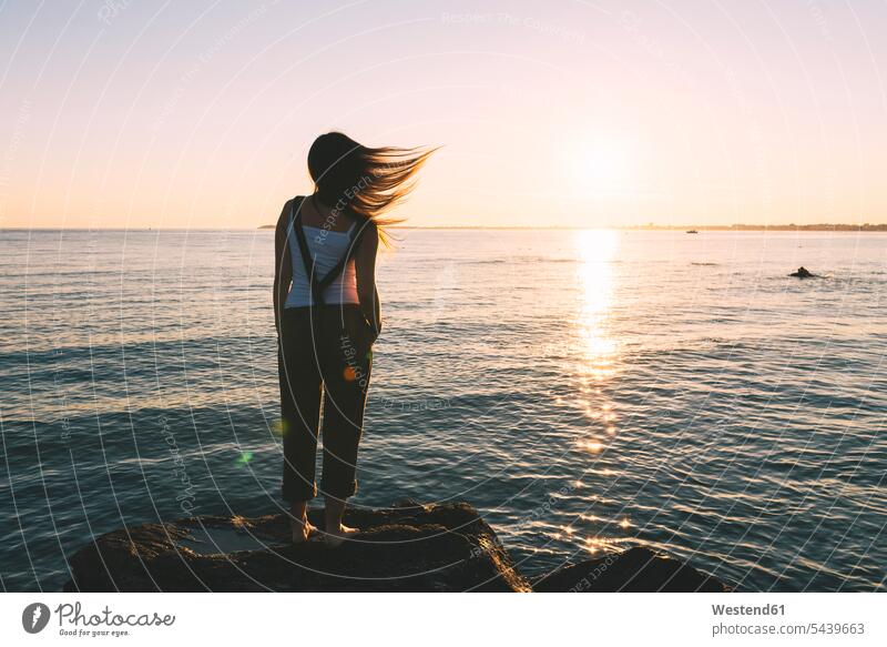 Frankreich, Pornichet, Frau mit wehendem Haar, die an der Strandpromenade steht und den Sonnenuntergang betrachtet Nur eine Frau 1 1 Frau Urlaub Ferien