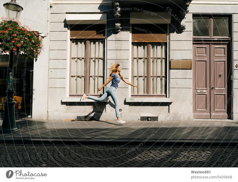 Niederlande, Maastricht, blonde junge Frau läuft entlang Gebäude in der Stadt staedtisch städtisch blonde Haare blondes Haar rennen weiblich Frauen Haus Häuser