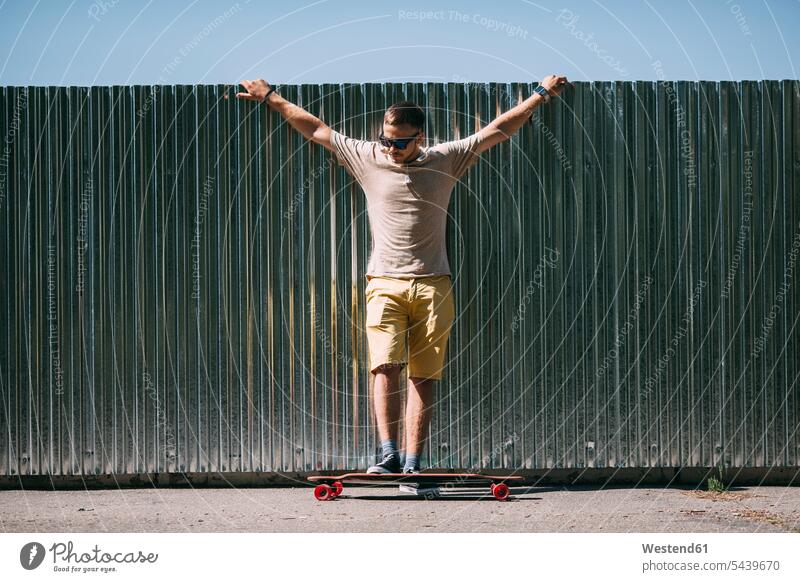 Junger Mann mit Longboard an einer Wand stehend Skateboard Rollbretter Skateboards Männer männlich steht Erwachsener erwachsen Mensch Menschen Leute People