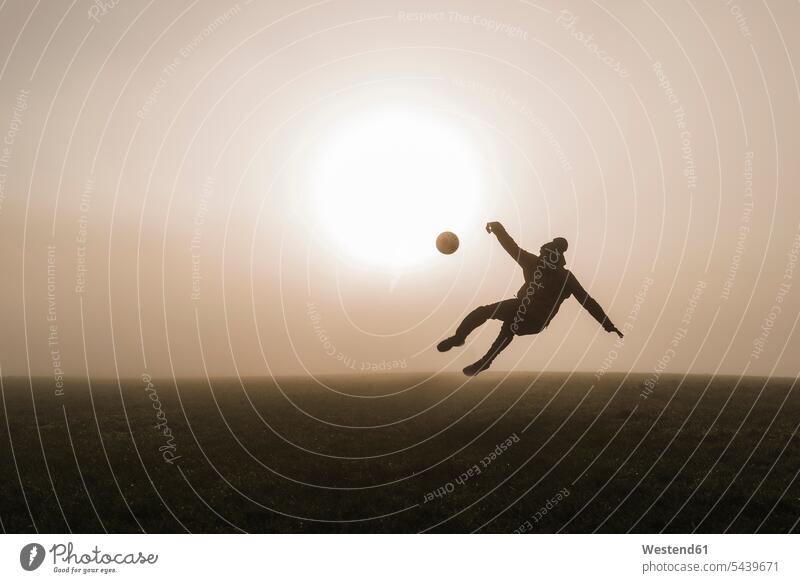 Junger Mann spielt abends auf der Wiese Fussball Europäer Kaukasier Europäisch kaukasisch Fußball Fußbälle Fußballwiese Fussballwiesen Fußballwiesen Sonne Abend
