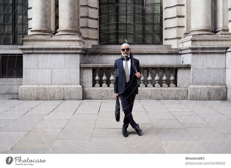 Großbritannien, London, Porträt eines stilvollen Geschäftsmannes mit Sonnenbrille und Regenschirm in Anzug und Krawatte Businessmann Businessmänner