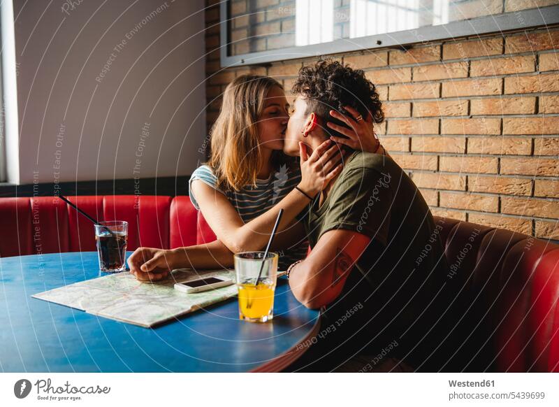 Junges Paar mit Karte küssend in einem Café sitzen sitzend sitzt Landkarte Landkarten Tisch Tische Cafe Kaffeehaus Bistro Cafes Cafés Kaffeehäuser Küsse Kuss