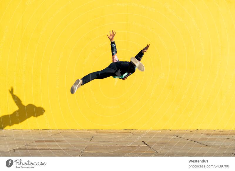 Akrobat springt Purzelbäume vor der gelben Wand Mauer Mauern gelber gelbes Salto Saltos Salti Akrobaten springen hüpfen Wände Waende Akrobatik Sport Sportler