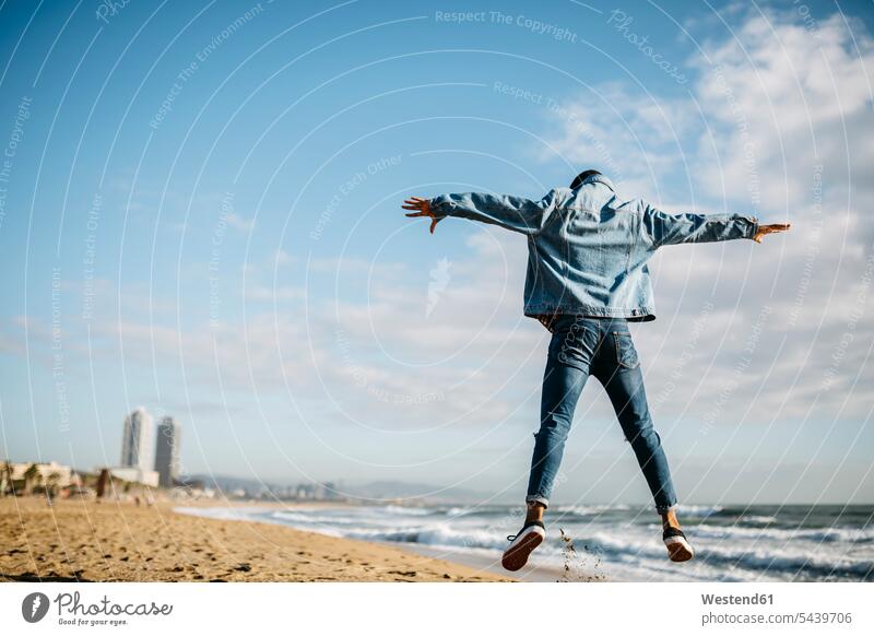 Spanien, Barcelona, Rückenansicht eines jungen Mannes, der am Strand in die Luft springt Beach Straende Strände Beaches Männer männlich springen hüpfen