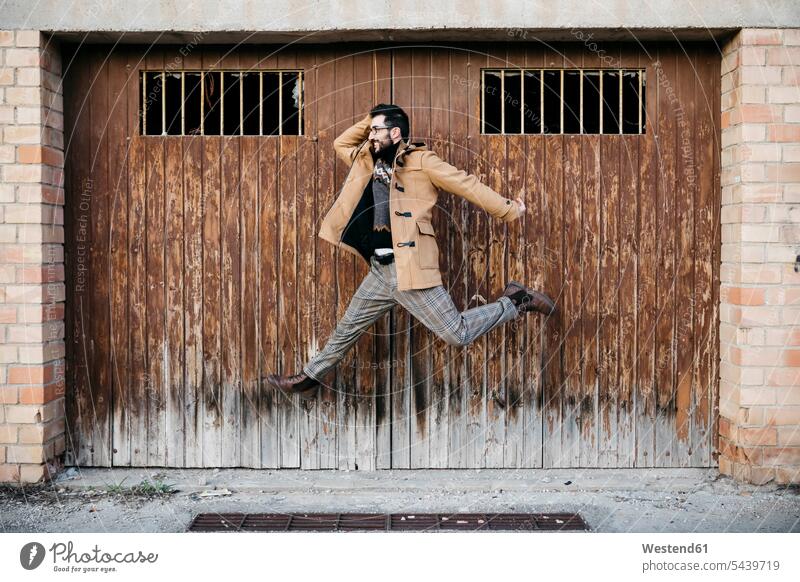 Spanien, Igualada, glücklicher Mann springt in der Luft an heruntergekommenem Holztor Stadt Holztür Holztueren Holztüren springen hüpfen Männer männlich Glück