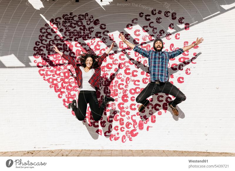 Glückliches junges Paar springt mit Herz vor eine Ziegelmauer Tarragona in der Luft Backstein Gemeinsamkeit zusammen gemeinsam Arm ausgestreckt Arme ausstrecken