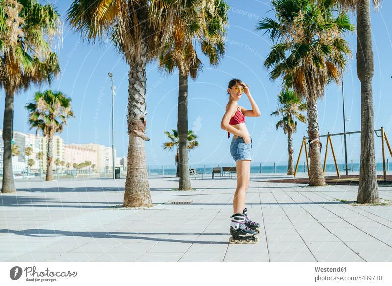 Junge Frau auf Inline-Skates auf einer Strandpromenade mit Palmen Inlineskates Inline skates inline skate Inliner weiblich Frauen Rollerblades Inlineskaten