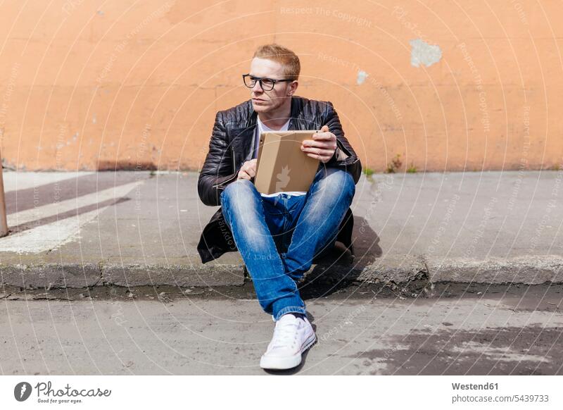 Junger Mann mit digitalem Tablet am Bordstein sitzend Männer männlich sitzt Tablet Computer Tablet-PC Tablet PC iPad Tablet-Computer Erwachsener erwachsen