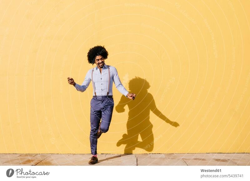 Lächelnder Mann tanzt vor einer gelben Wand Männer männlich Mauer Mauern gelber gelbes tanzen tanzend lächeln Erwachsener erwachsen Mensch Menschen Leute People