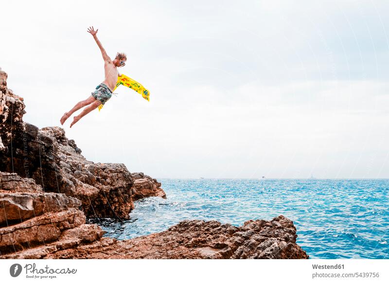 Mann mit Luftmatratze springt von Felsen ins Meer springen hüpfen Meere Männer männlich Sprung Spruenge Sprünge Gewässer Wasser Erwachsener erwachsen Mensch