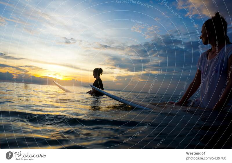 Indonesien, Bali, Canggu, zwei Surferinnen im Wasser, die die Sonne beobachten Dunkelheit Erholung erholen Silhouette Umrisse Gegenlicht Kontur Silhouetten