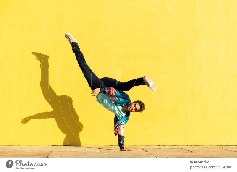 Acrobat beim Bewegungstraining vor einer gelben Wand üben ausüben Übung trainieren Selbstverwirklichung Ganzkörperansicht Ganzansicht Ganzkörperaufnahme
