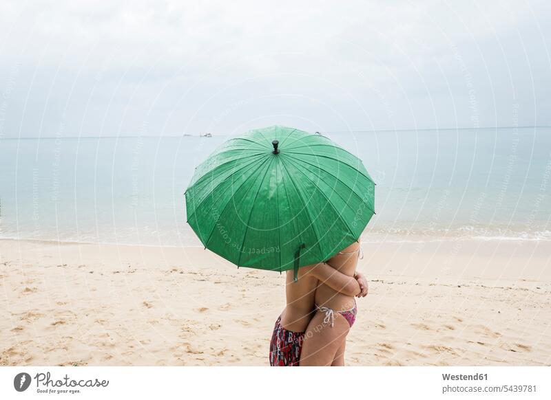 Thailand, Junge umarmt seine Mutter am Strand unter einem grünen Regenschirm Mamas Mami Mutti Mütter Muetter Mamis Muttis Buben Knabe Jungen Knaben männlich