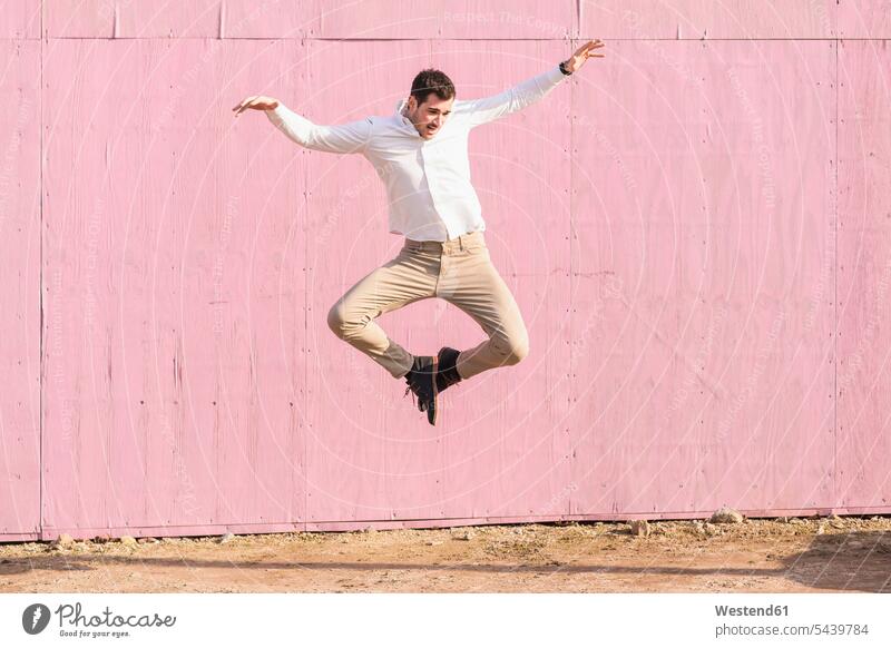 Überschwänglicher junger Mann, der vor einer rosa Wand springt springen hüpfen Männer männlich Wände Waende rosafarben ausgelassen Ausgelassenheit Sprung