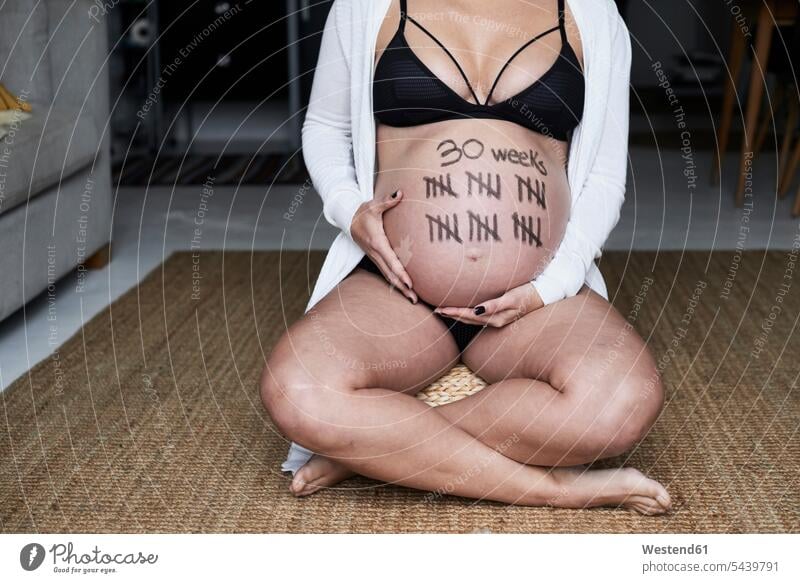 Nahaufnahme einer schwangeren Frau, die zu Hause auf dem Boden sitzt, mit Strichmännchen auf ihrem Bauch Bäuche Böden Boeden weiblich Frauen Schwangere